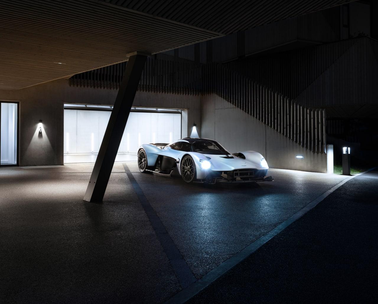 A pale Valkyrie rests inside a dark modern garage crossed by structural beams. Glass doors and small lamps extend the interior beyond the car. Source: 4kwallpapers.com. Original artist not identified by the source page.