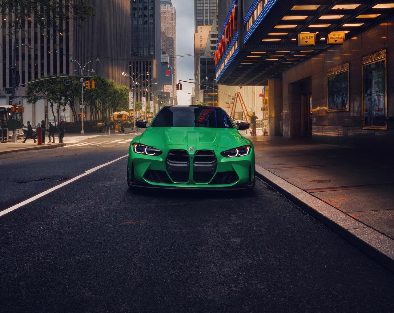 A green M4 faces the viewer beneath a projecting urban canopy. Stone facades, pavement lines and warm window light extend down both sides of the street. Source: 4kwallpapers.com. Original artist not identified by the source page.