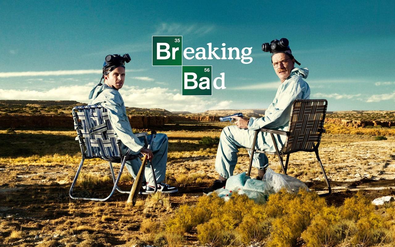 Walter and Jesse sit in folding chairs wearing protective gear in an open desert. Dry scrub, low hills and a turquoise sky contrast with the makeshift setup. Source: sarendg on Wallpapers.com. Original artist not identified by the page.