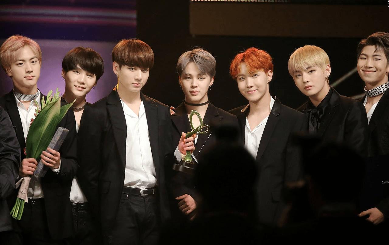 Seven members in dark suits stand across the frame holding awards.