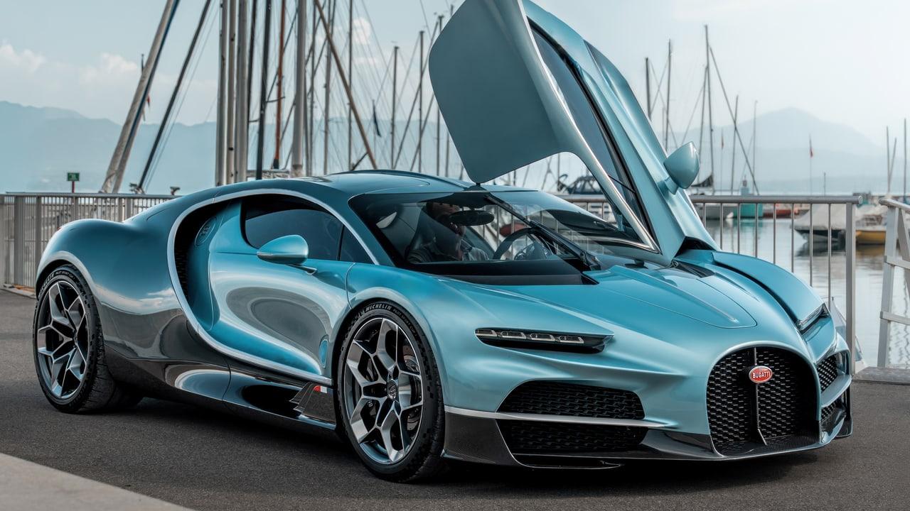 A blue Tourbillon stands with its doors raised beside a marina. Masts, waterfront railings and the car's curved body fill the landscape. Source: 4kwallpapers.com. Original artist not identified by the source page.