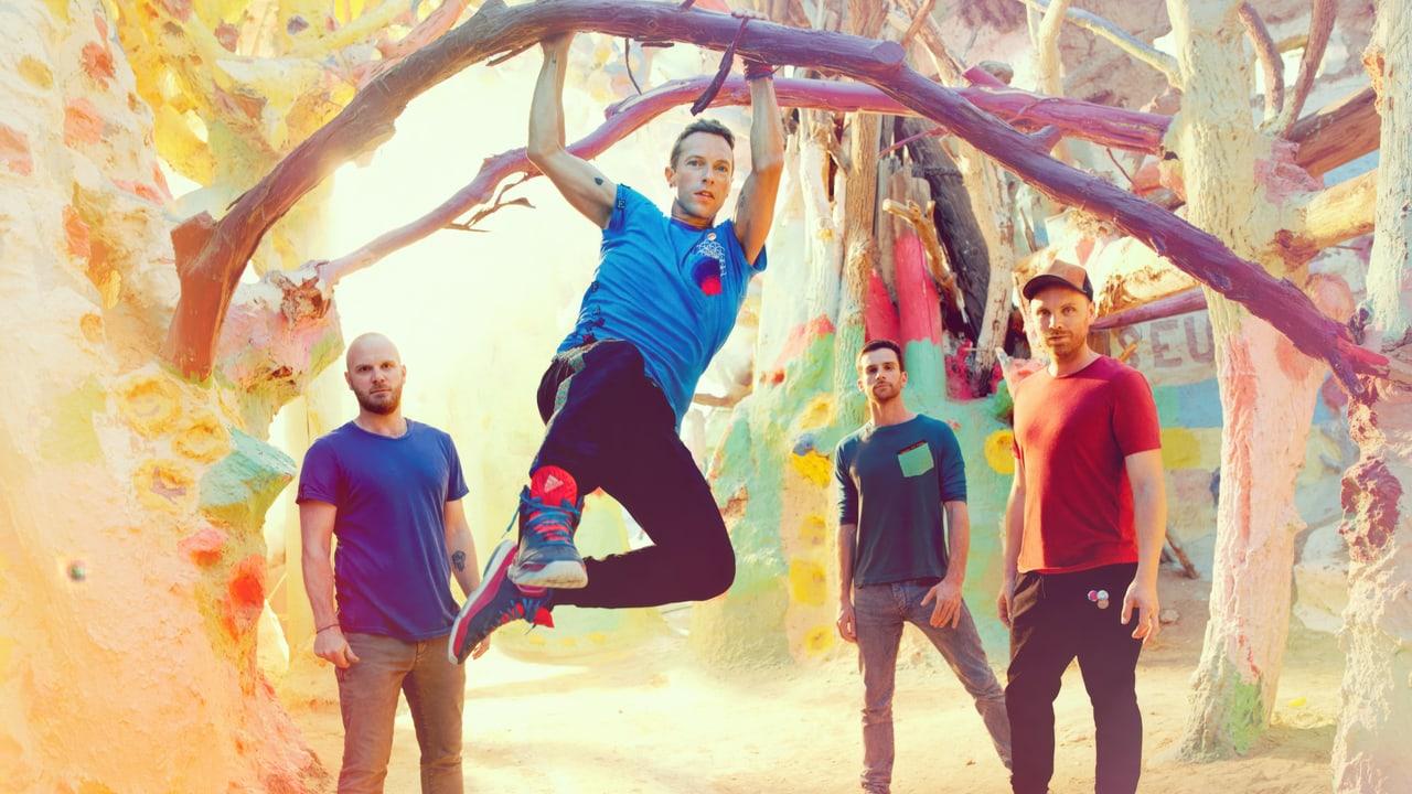 Coldplay poses among painted trees and pastel-colored scenery with Chris Martin caught mid-jump. Branches and bright textures fill the backdrop. Source: 4kwallpapers.com. Original artist not identified by the source page.