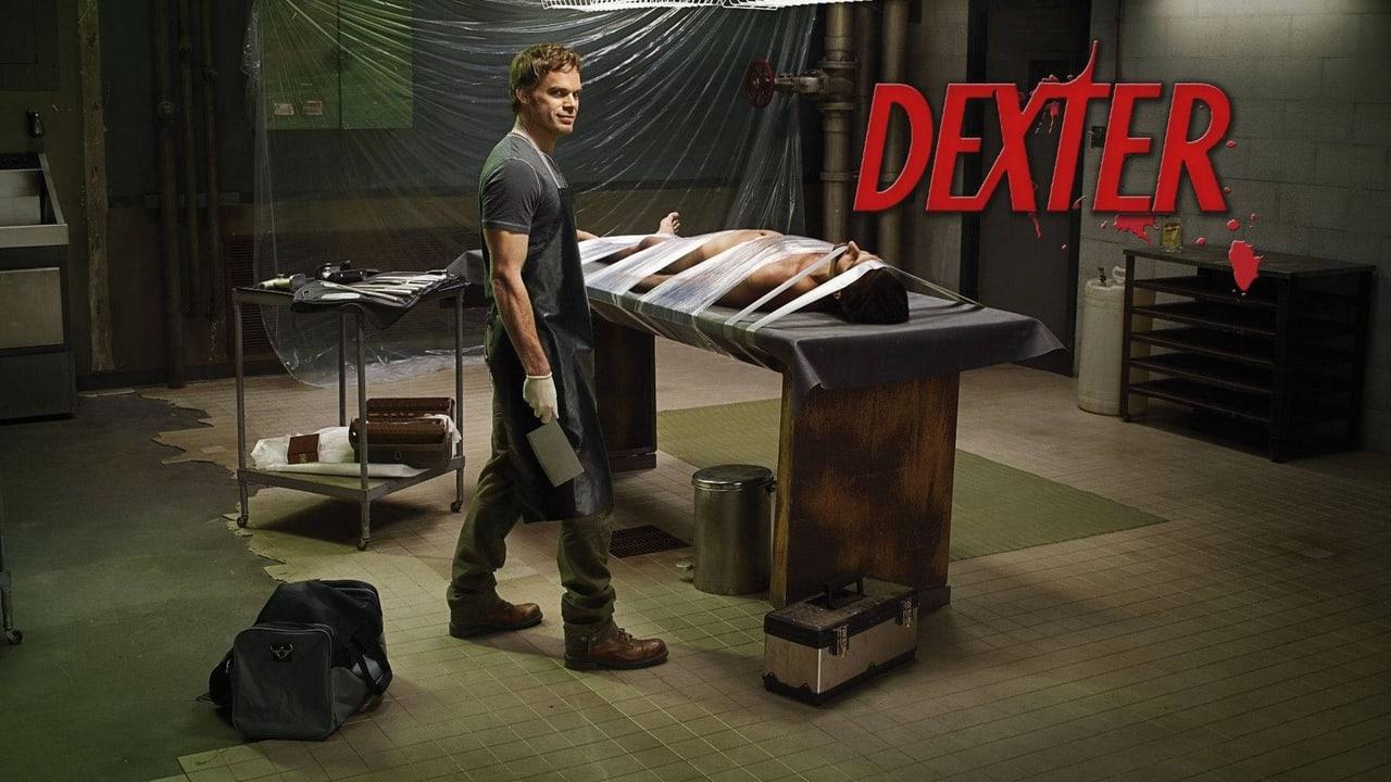 Dexter stands in a dim workroom with a covered table, plastic sheeting and utility carts. Tiled walls, tools and shelving retain the room at both margins.