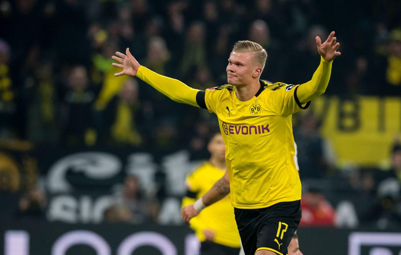 Haaland opens his arms in a historic yellow Dortmund shirt against dark stands. Supporters and yellow banners retain the club context around the pose. Source: cunaked on Wallpapers.com. Original artist not identified by the page.