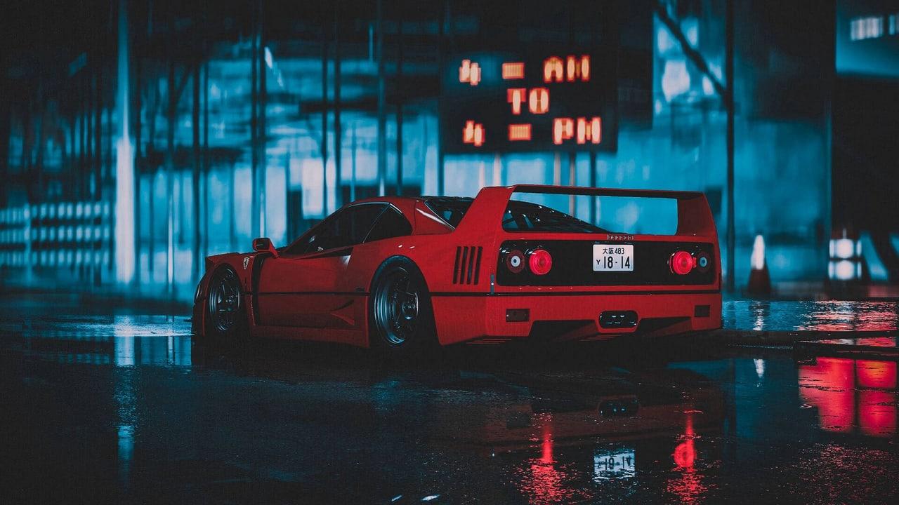 A red Ferrari F40 sits outside a glass-fronted building reflected in wet pavement at night.