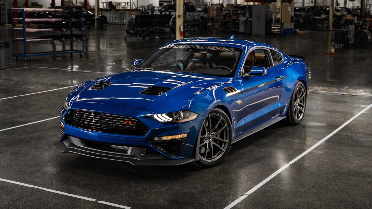 A blue Mustang sits on a polished workshop floor. Tool racks, benches and marked bays extend beyond the car to both edges.