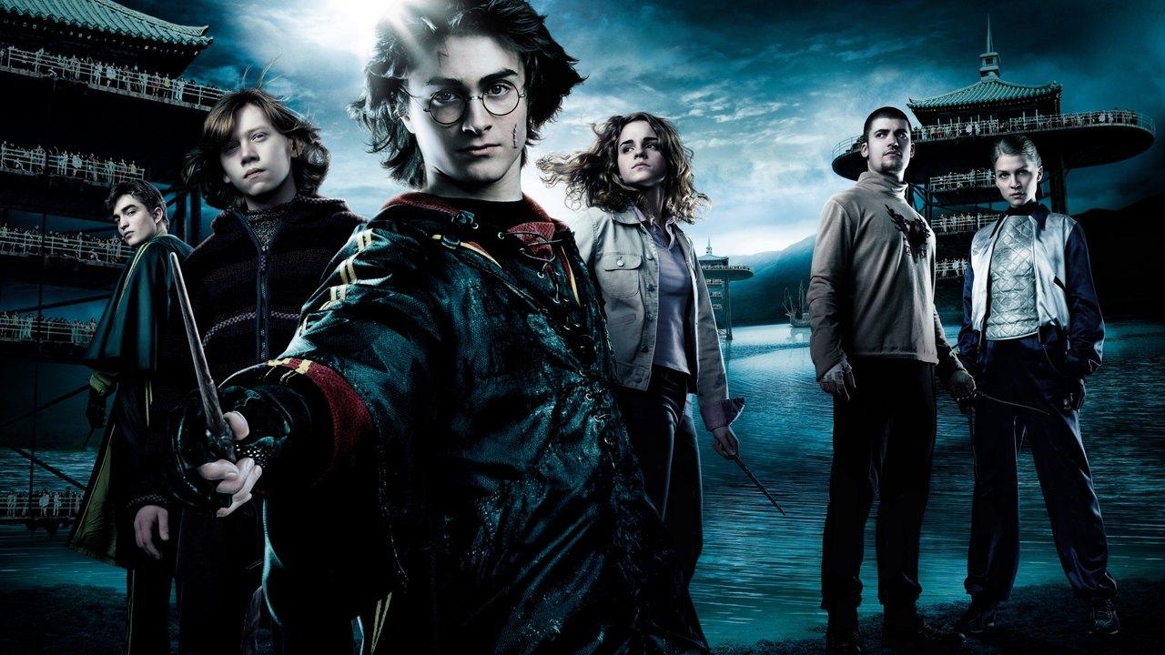 Harry, Ron, Hermione and fellow students stand beside a dark lake with tall spectator stands beneath a stormy sky.