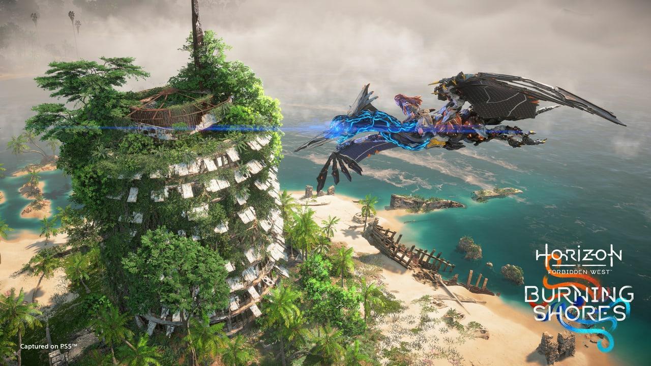 An overgrown tower rises beside turquoise coastal water as Aloy rides a flying machine. Vegetation on the left and the machine wing and shore on the right keep the vista expansive.