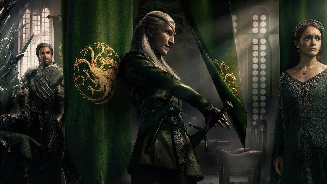 An ensemble in dark green costumes stands beneath green dragon banners and pale castle windows.