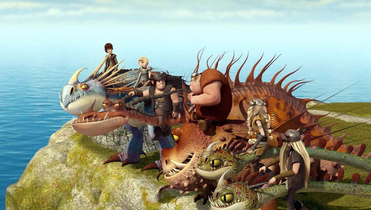 Hiccup and the dragon riders gather on a grassy cliff above a bright blue sea. Horns, tails and the coastline spread the group across the wallpaper. Source: nipper on Wallpapers.com. Original artist not identified by the page.