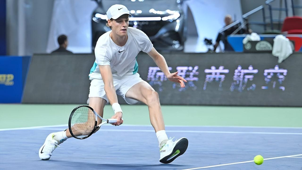 Sinner stretches for a low ball on a pale blue hard court in a white-and-mint kit. Court lines, equipment and the ball carry the action across the scene. Source: m.gettywallpapers.com. Original artist not identified by the source page.