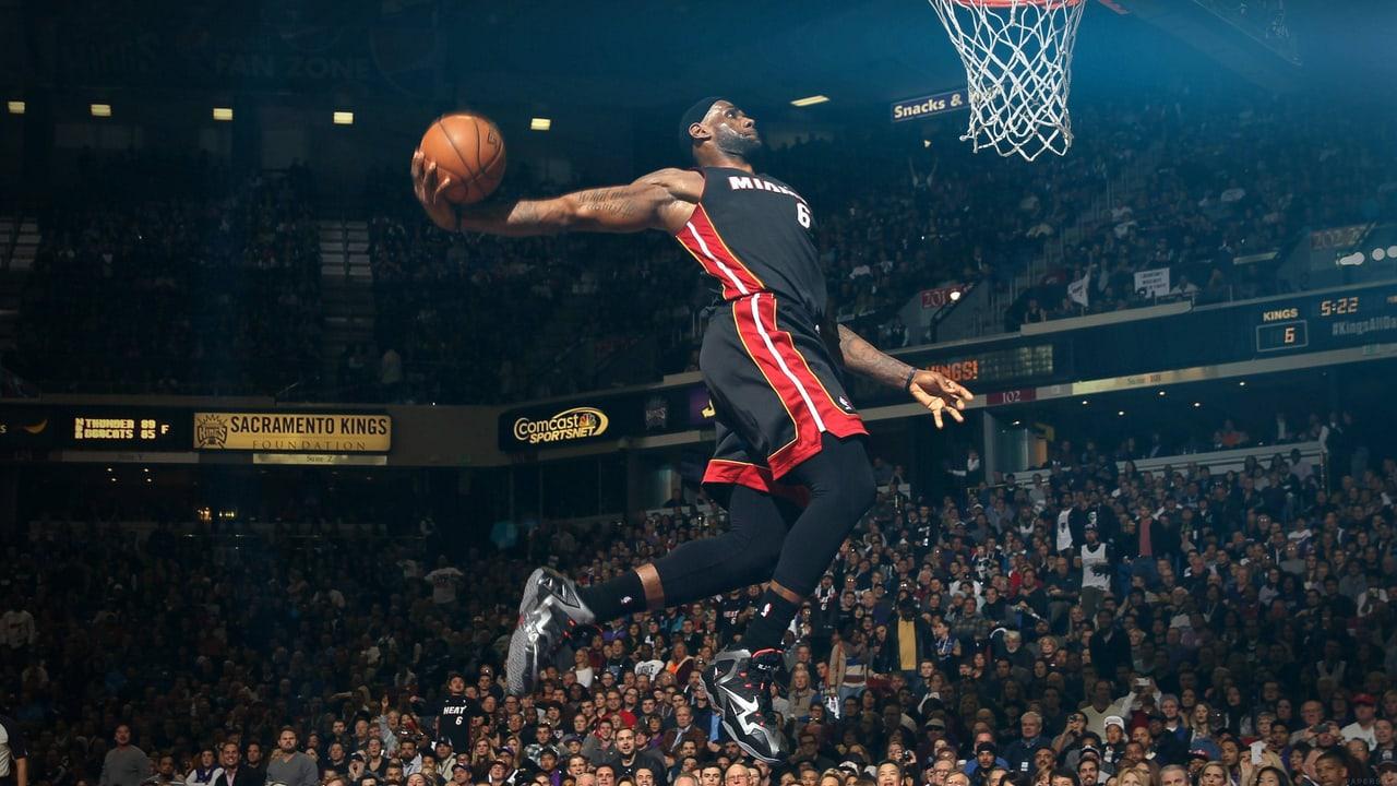 LeBron stretches toward the rim in a historic Miami uniform above a darkened crowd. Arena signage and rows of spectators hold the surrounding space. Source: allyn on Wallpapers.com. Original artist not identified by the page.