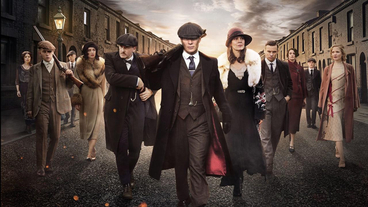 The Shelby ensemble walks between brick terraces under an overcast sky. Period coats, cobbles and gas lamps fill the width of the street. Source: 4kwallpapers.com. Original artist not identified by the source page.