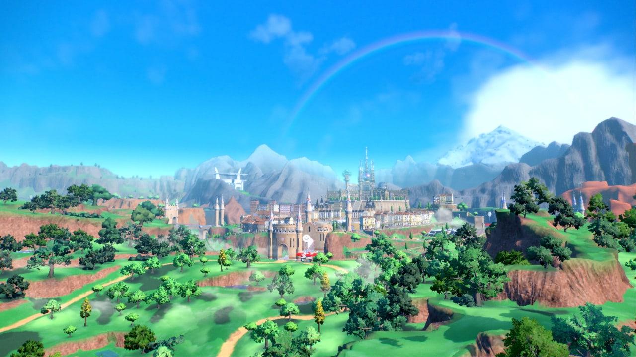 Green fields, reddish cliffs and a distant castle city spread beneath a bright blue sky and rainbow.