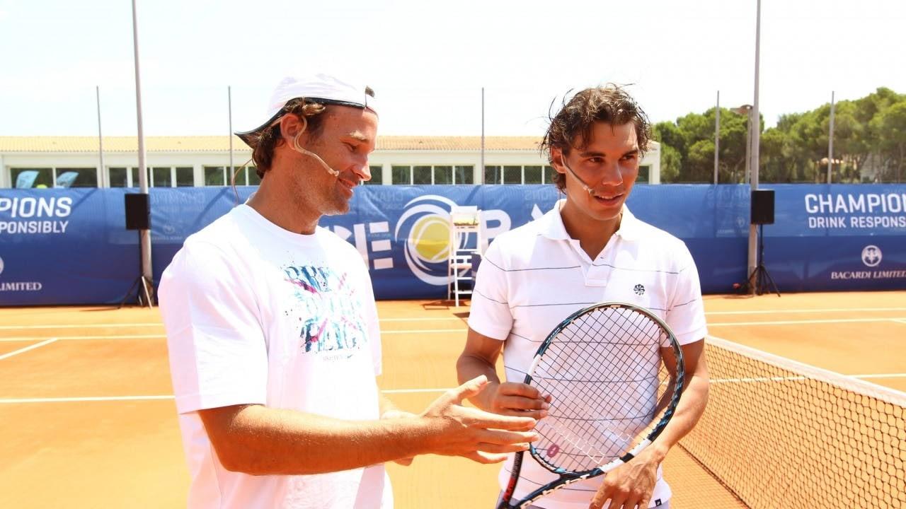 Rafael Nadal stands beside another player during a clay-court appearance. The net, court lines and background buildings remain visible outside the central figures.