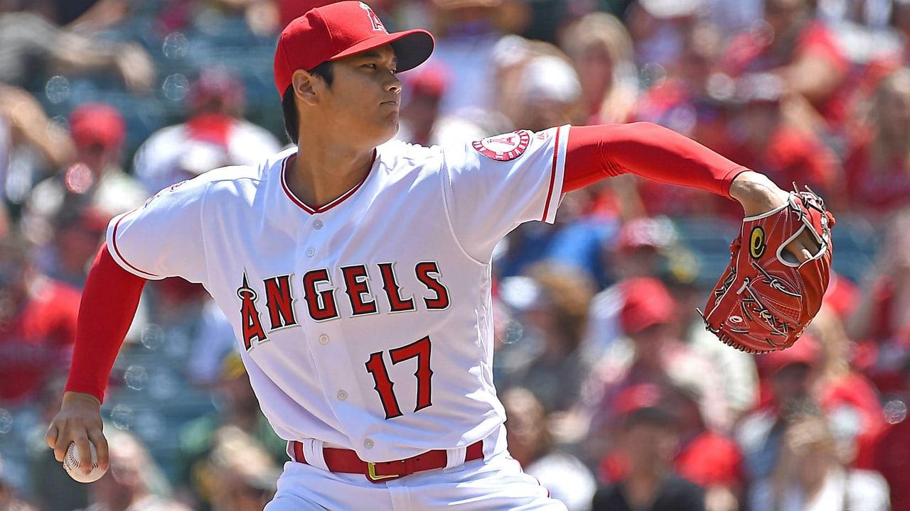 Shohei Ohtani prepares to pitch in a historical white Angels number 17 uniform. His arm and glove reach toward opposite edges before a sunlit crowd.