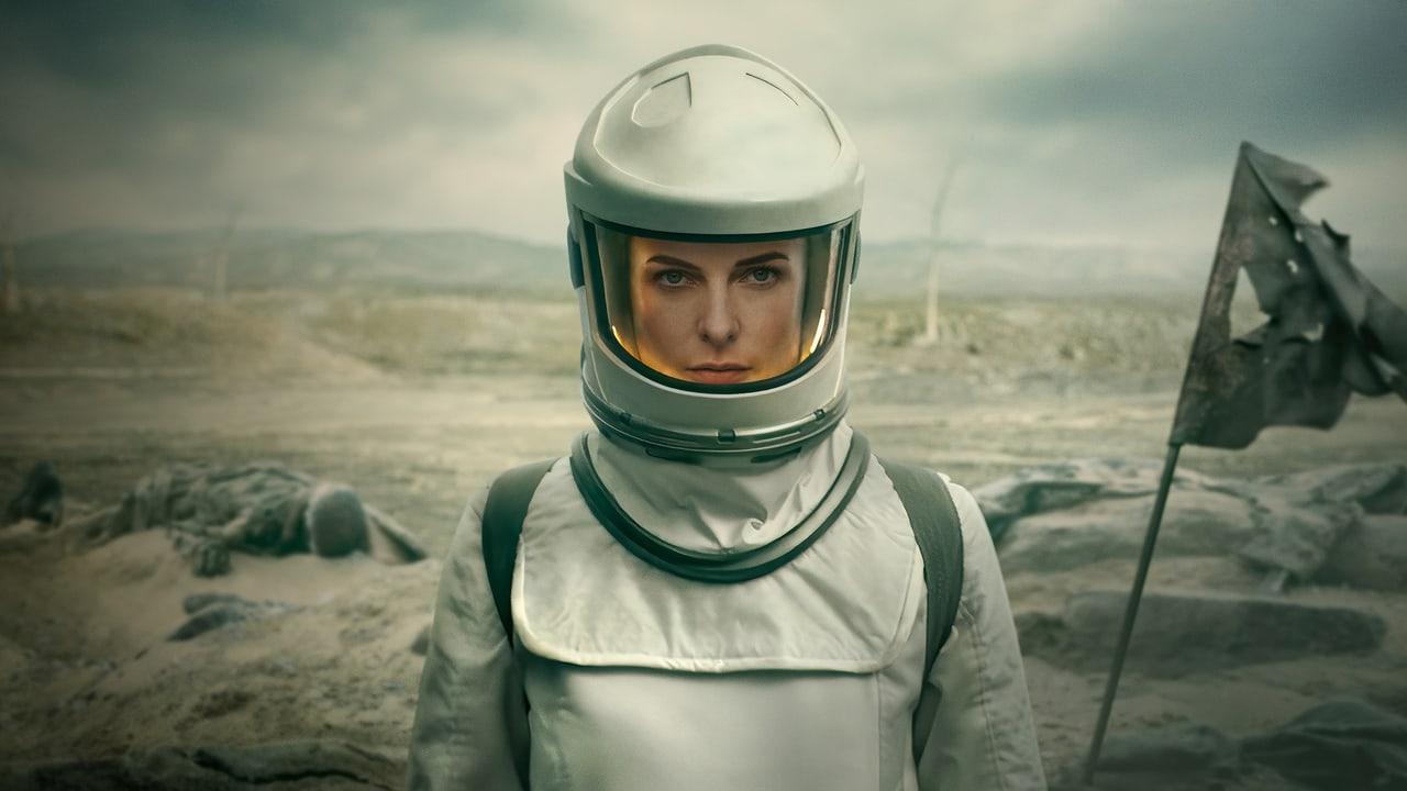 A protective suit stands in a desaturated wasteland beside a battered flag. Low ruins and barren ground stretch across the frame beneath a pale, polluted sky. Source: 4kwallpapers.com. Original artist not identified by the source page.