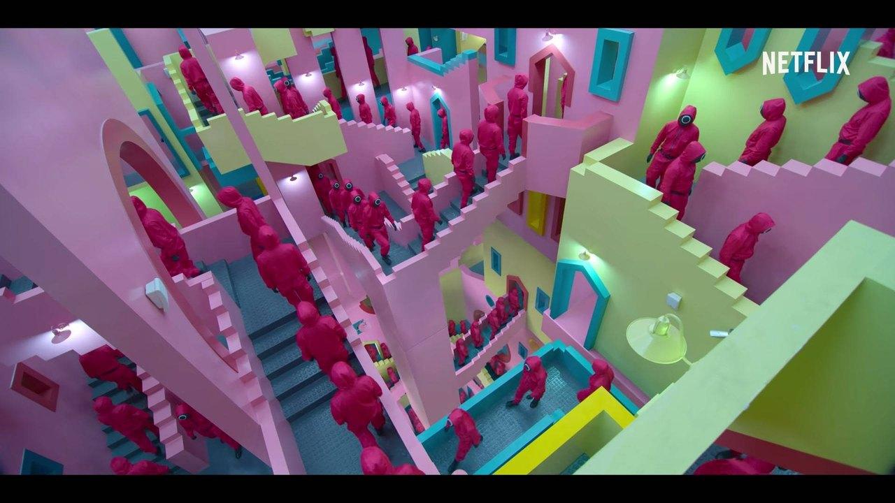 Pink-suited guards move through a maze of pink, mint and turquoise staircases; the Netflix mark remains visible.