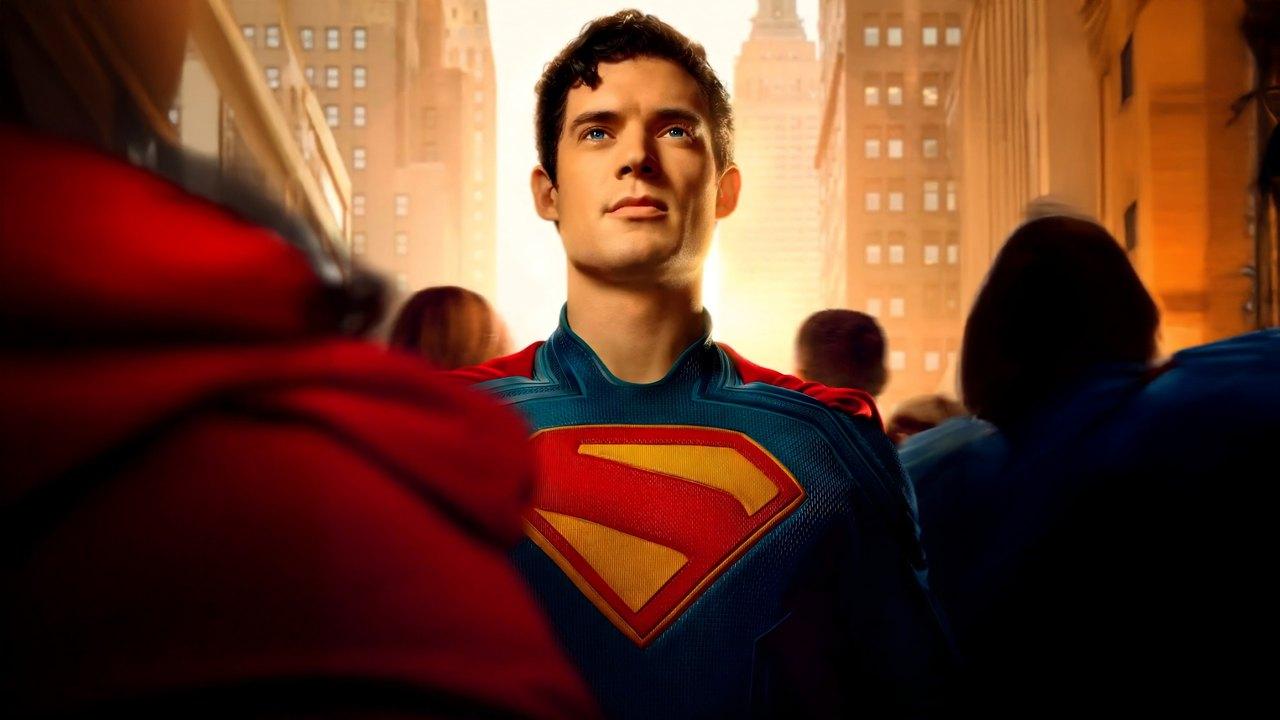 Superman stands in a warmly lit city street, surrounded by people and tall buildings.