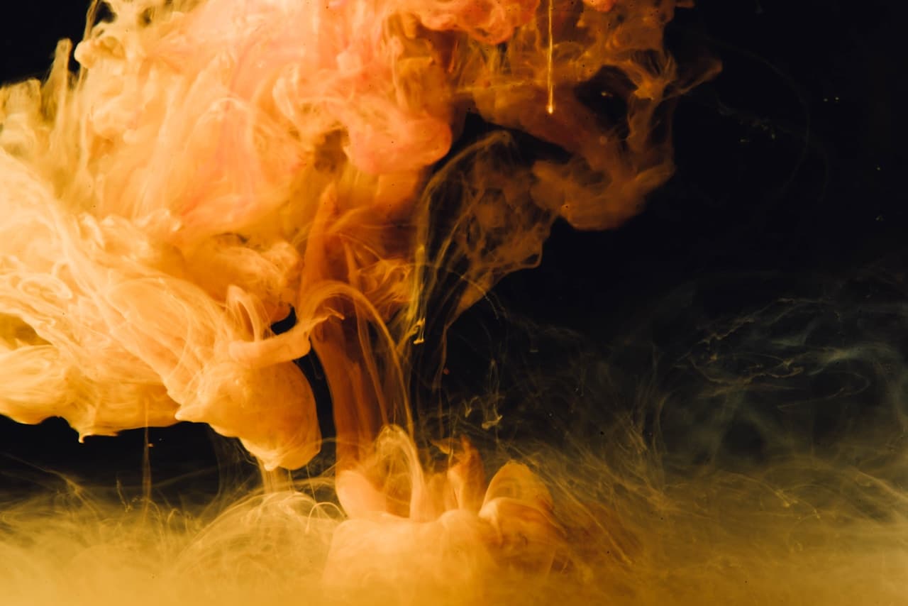 A dramatic abstract scene where a bright orange-gold smoke cloud rolls through a deep black background. The plume is dense and textured, with billowing curls and softer edges fading into darkness. Subtle greenish and brown undertones appear in the shadows, adding depth to the warm glow. The composition is asymmetrical, with the luminous smoke occupying one side and large negative space on the other, creating tension and focus. Low-key lighting and rich contrast make the mood intense, mysterious, and cinematic.