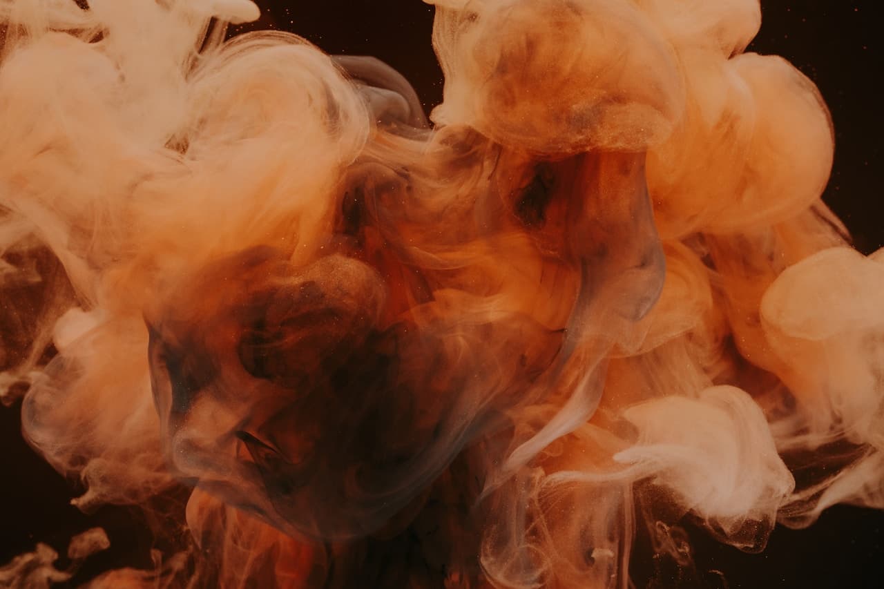 A dark, atmospheric abstract where swirling smoke forms suggestive, human-like contours. Warm amber and orange plumes billow above a deeper shadowed core, while pale white smoke wraps around the lower area like mist. The shapes resemble a profile or head-like silhouette without revealing any identity, giving the scene a surreal, illustrative quality. The composition is centered and dramatic, with low-key lighting that highlights the smoke's layered texture and keeps the background nearly black. Overall mood is mysterious and slightly cinematic, balancing warmth with shadow.