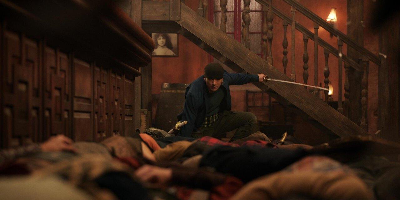 Zoro in a timber-lined fight scene Zoro holds a sword inside a dim room with wooden cupboards, a staircase and warm lamps.